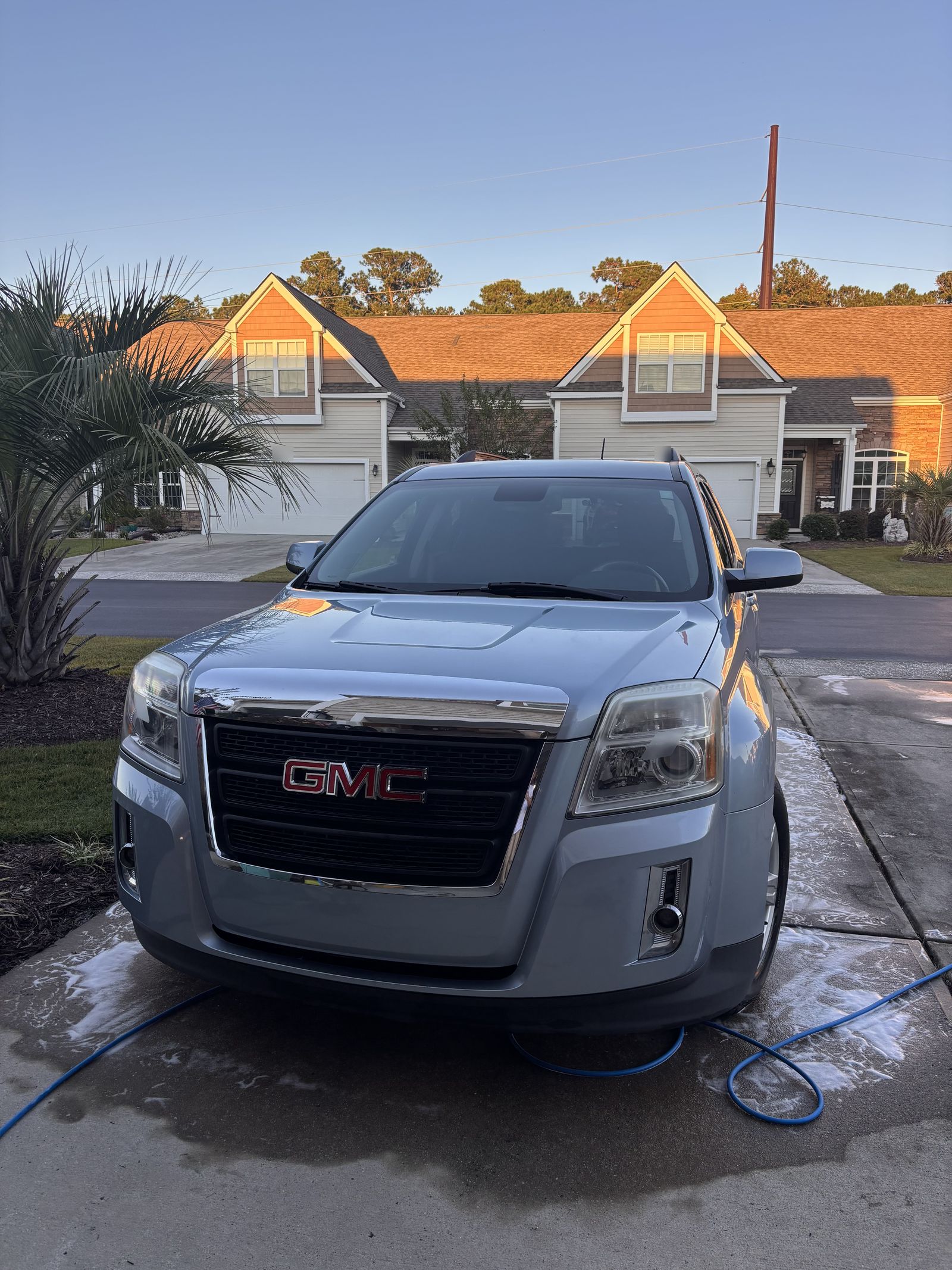 Freshly washed silver-blue GMC Terrain in a driveway at golden hour, hose on the wet concrete